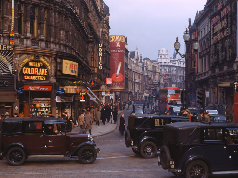 Fotografia histórica de Piccadilly Circus em Londres, com os letreiros da região e carros de época