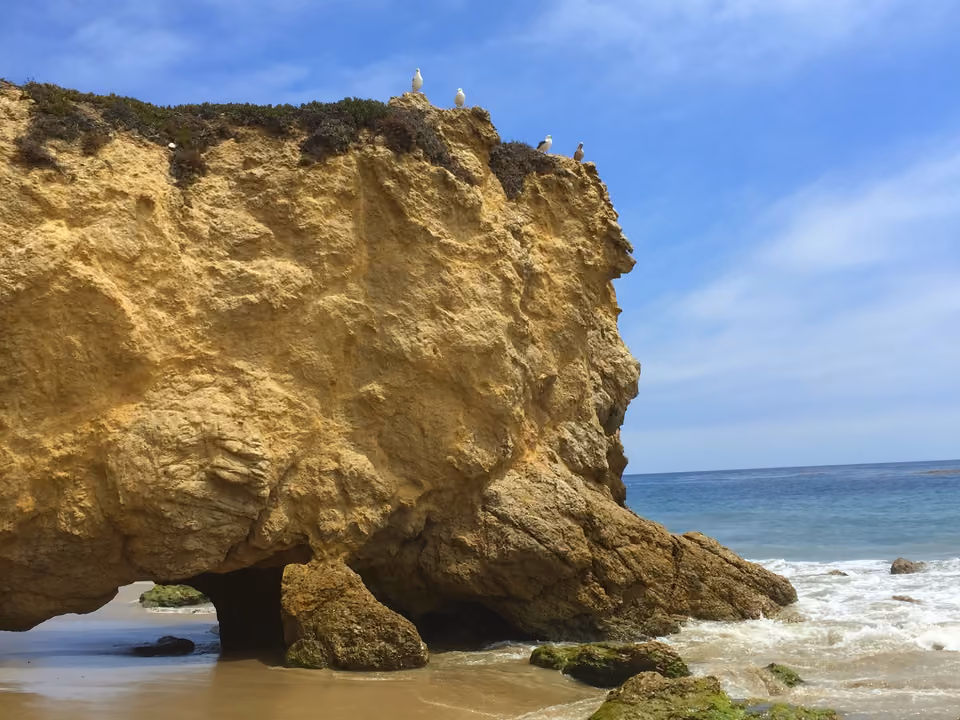 Praia de Malibu em Los Angeles, com falésias ao fundo e ondas do oceano Pacífico quebrando na areia