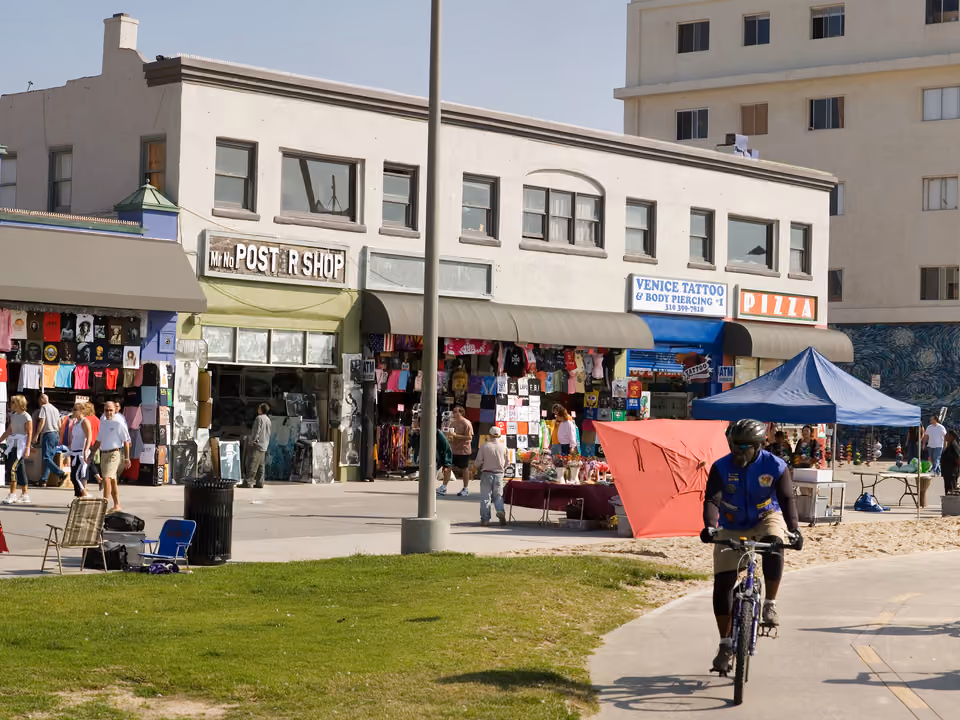 Calçadão de Venice Beach em Los Angeles, com quiosques coloridos, ciclistas e a praia ao fundo