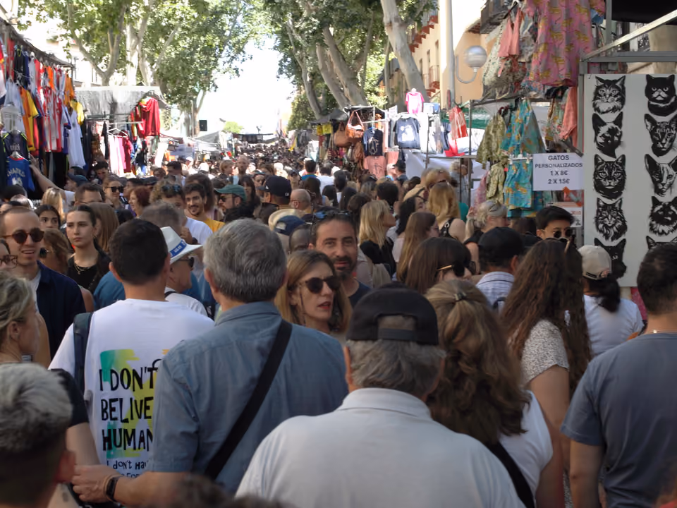 Feira de rua do El Rastro em Madri num domingo de manhã: multidão descendo a Ribera de Curtidores entre as barracas de roupa e antiguidades, sob os plátanos