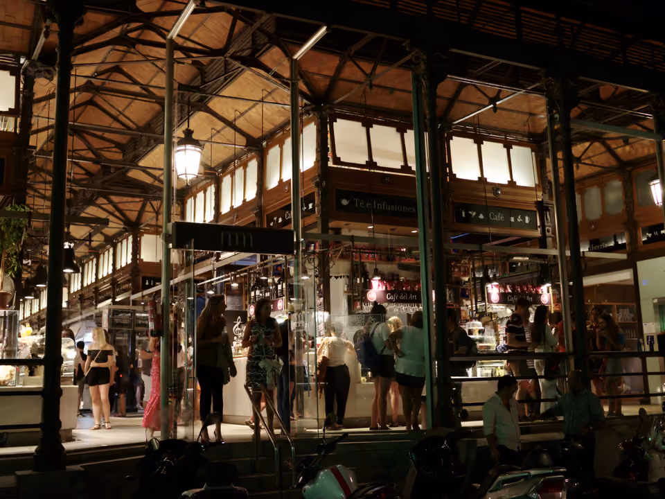 Mercado de San Miguel em Madri à noite, o galpão de ferro e vidro de 1916 iluminado por dentro, visto de fora com as bancas e o público no interior