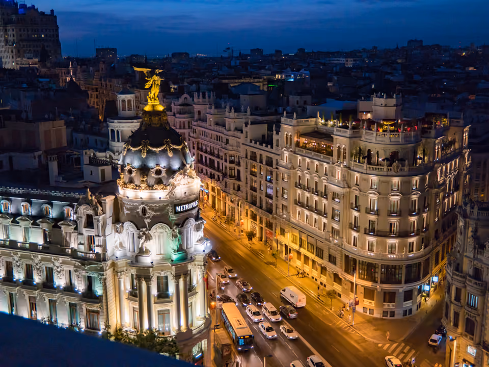 Início da Gran Vía de Madri na hora azul, com o edifício Metrópolis e sua estátua alada dourada iluminados e a avenida de prédios monumentais descendo ao fundo