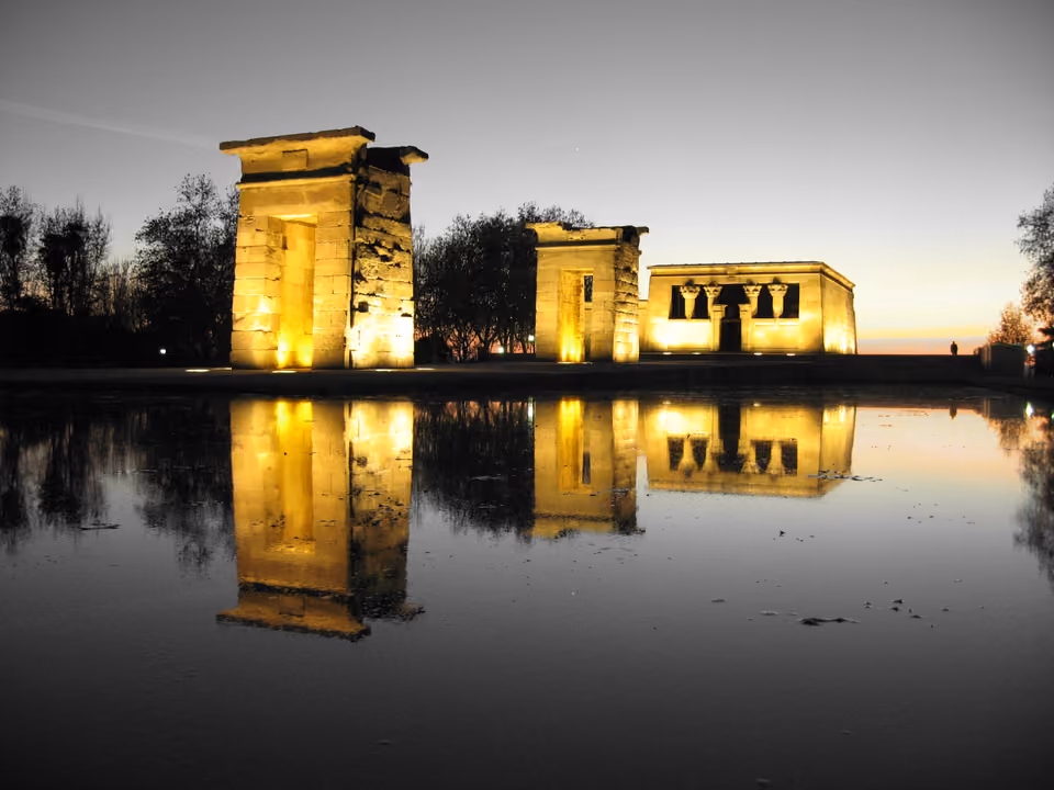 Templo de Debod em Madri ao anoitecer, o templo egípcio de pedra iluminado e refletido no espelho d'água, com o céu em degradê no horizonte