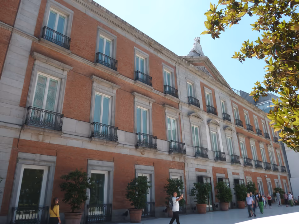 Fachada avermelhada do Palácio de Villahermosa, sede do Museo Thyssen-Bornemisza, com suas sacadas de ferro e os vasos de árvores na calçada do Paseo del Prado
