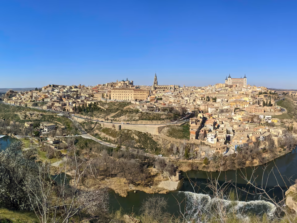 Cidade histórica de Toledo sobre a colina, cercada pela curva do Rio Tejo, com o Alcázar e a torre da catedral no alto, vista do mirador do outro lado do rio