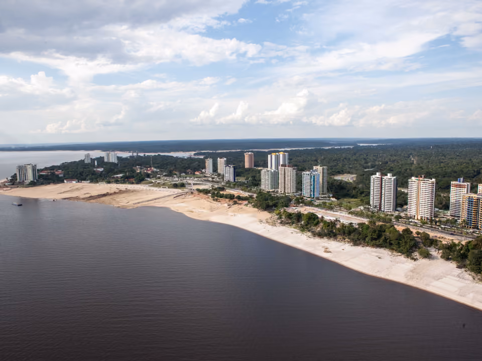 Vista aérea da orla da Praia da Ponta Negra em Manaus, com faixa de areia às margens do Rio Negro e prédios ao fundo