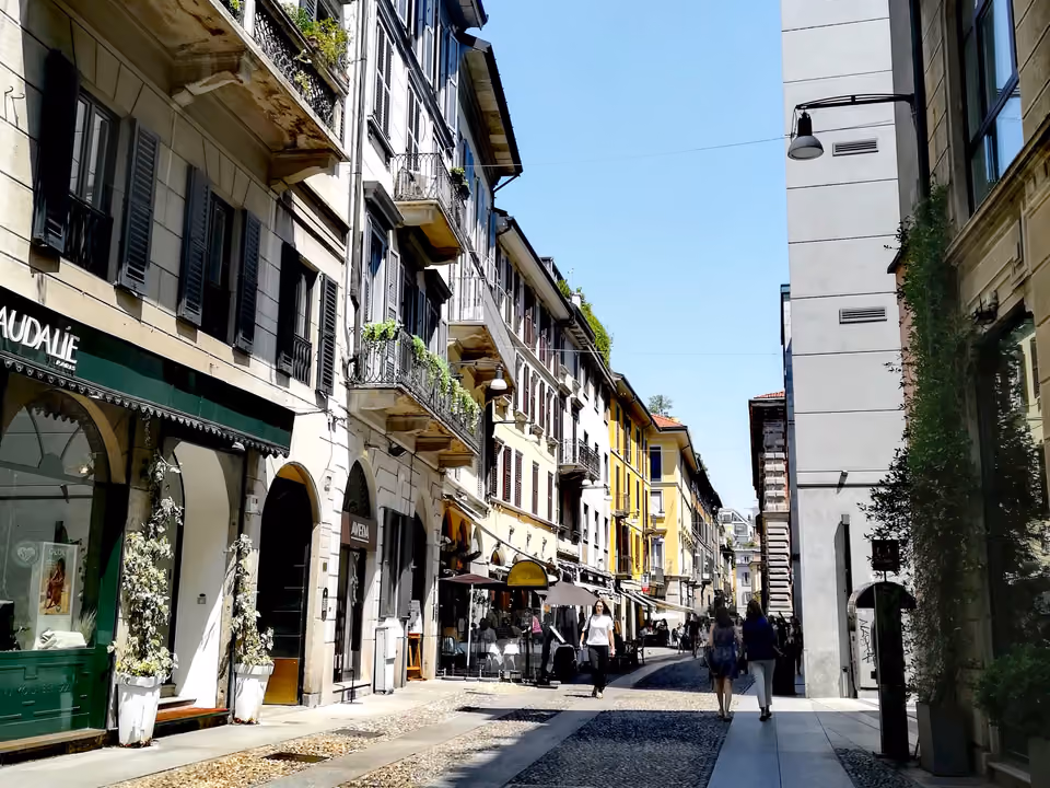 Rua de pedestres do bairro de Brera, com paralelepípedo, fachadas em tons pastel com venezianas e mesas de café na calçada