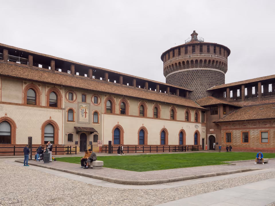 Pátio interno do Castello Sforzesco, com a muralha ameada de tijolo, um torreão redondo e a ala de museu com janelas ogivais