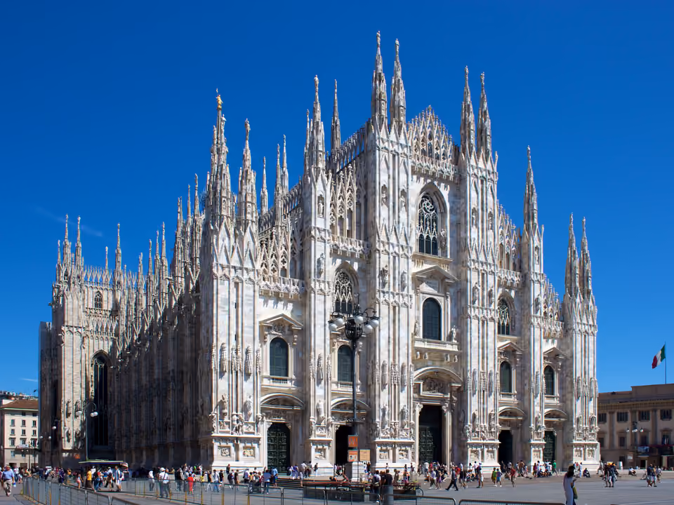 Fachada e flanco do Duomo de Milão em ângulo, catedral gótica de mármore branco com centenas de pináculos sob céu azul