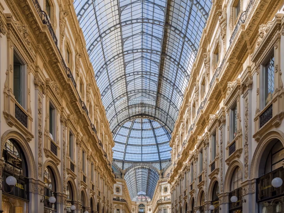 Interior da Galleria Vittorio Emanuele II, arcada de vidro e ferro entre palácios ornamentados, com a cúpula central ao fundo