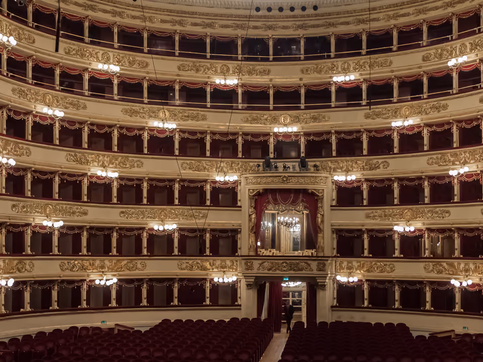 Sala em ferradura do Teatro alla Scala vista do palco, com os camarotes forrados de vermelho e ouro em vários níveis e o camarote real ao centro