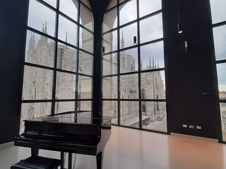 Sala do Museo del Novecento com janelas em arco emoldurando a lateral do Duomo, e um piano de cauda em primeiro plano