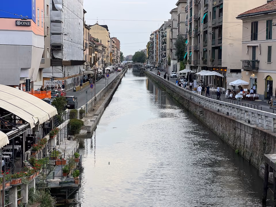 Canal do Naviglio Grande ao entardecer, com terraços de restaurante e guarda-sóis brancos nas duas margens