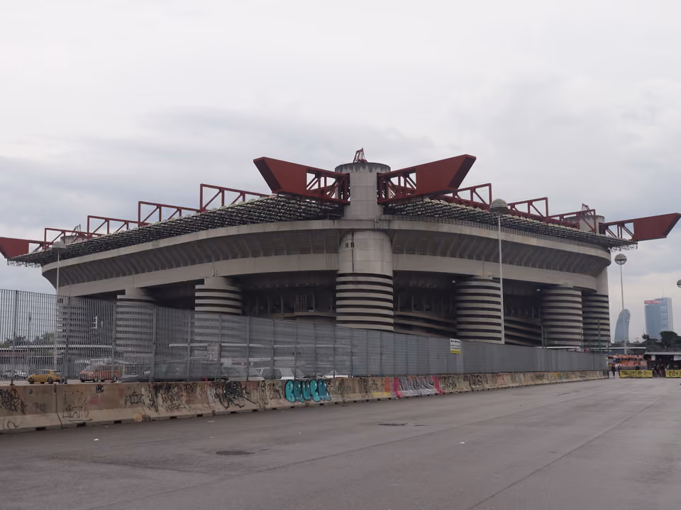 Fachada do estádio San Siro de Milão, com as rampas helicoidais nas torres de canto e a estrutura de vigas vermelhas no alto