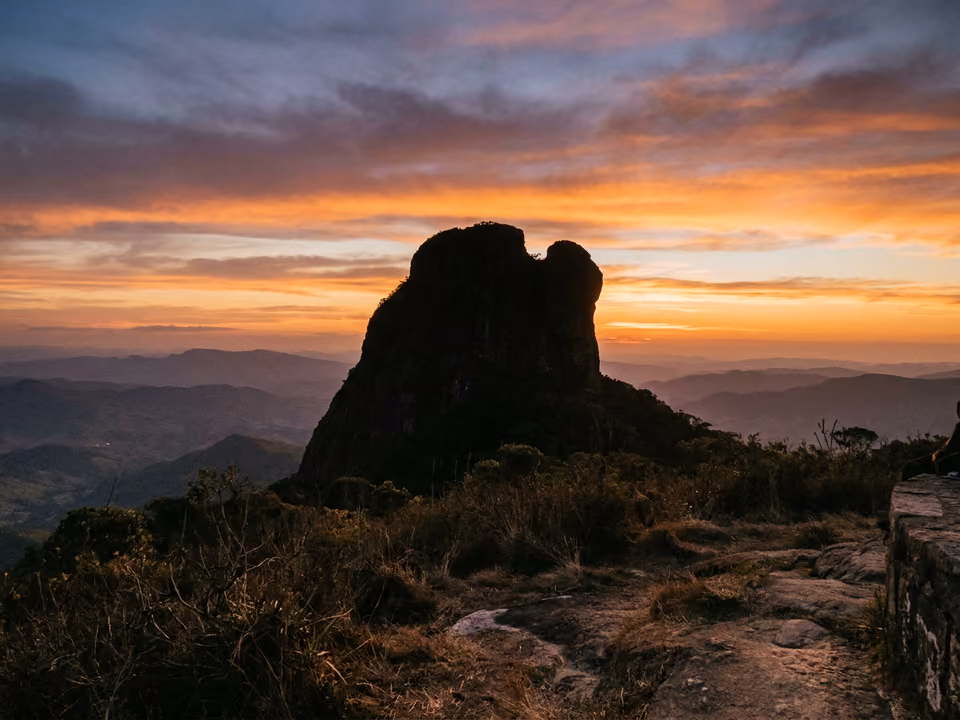 Formação rochosa do Chapéu do Bispo em silhueta contra o céu alaranjado do pôr do sol