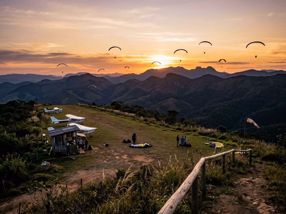 Pista de grama do mirante do aeroporto ao pôr do sol, com parapentes sobre a serra