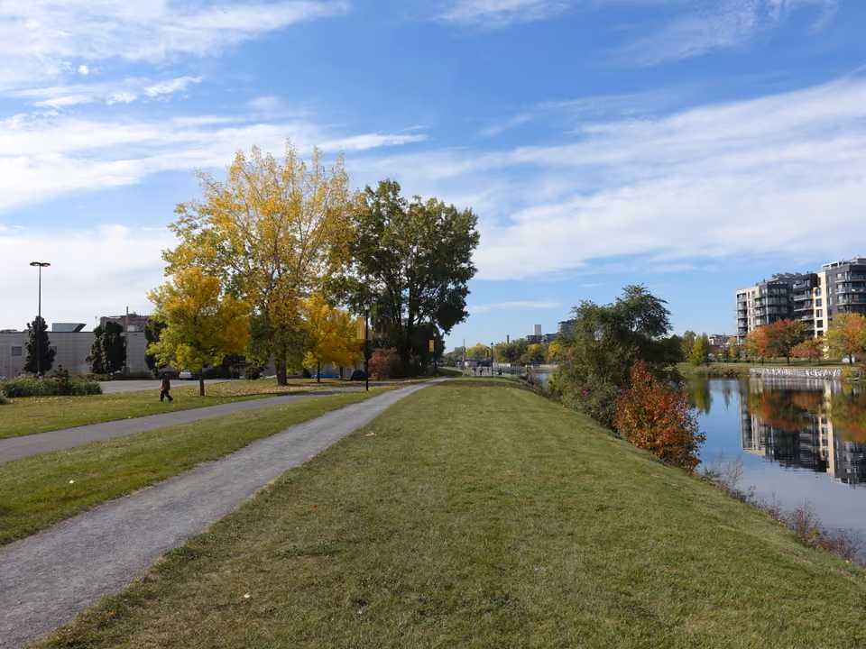 Ciclovia à beira do Canal de Lachine, em Montreal, com o canal e antigos armazéns industriais ao fundo