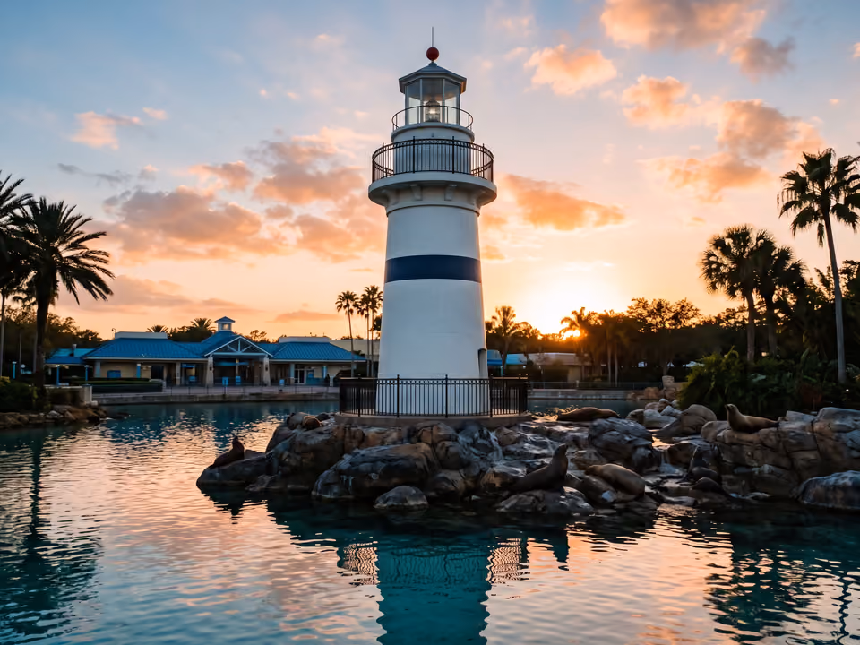 Farol branco e azul-marinho na entrada do SeaWorld Orlando sobre rochas com leões-marinhos, ao entardecer