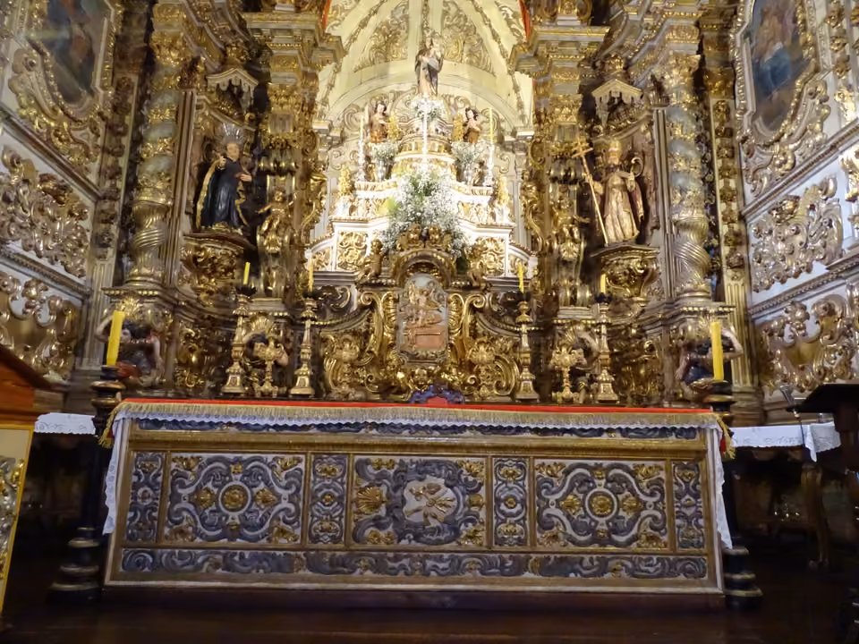 Altar-mor da Igreja de Nossa Senhora do Pilar em Ouro Preto, coberto de talha barroca folheada a ouro, com imagens de santos, velas e um frontal de altar em azulejo