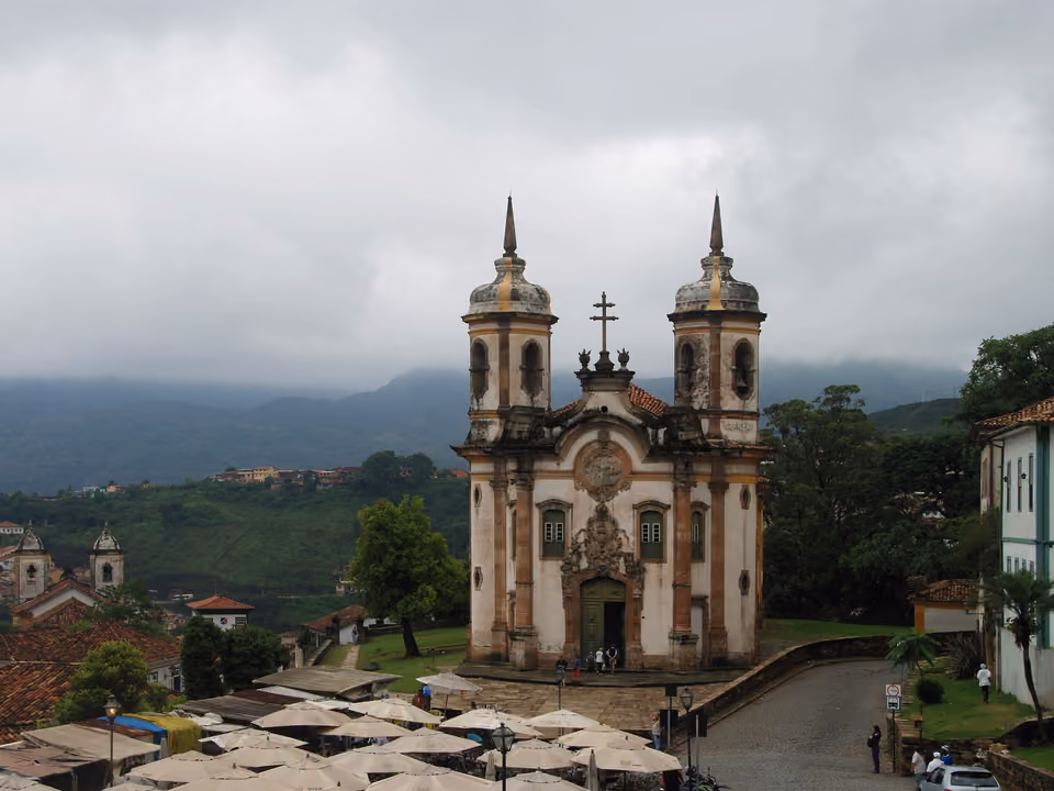 Igreja de São Francisco de Assis em Ouro Preto vista do Largo de Coimbra, com as duas torres cilíndricas, o portal esculpido e as barracas da feira de pedra-sabão em primeiro plano