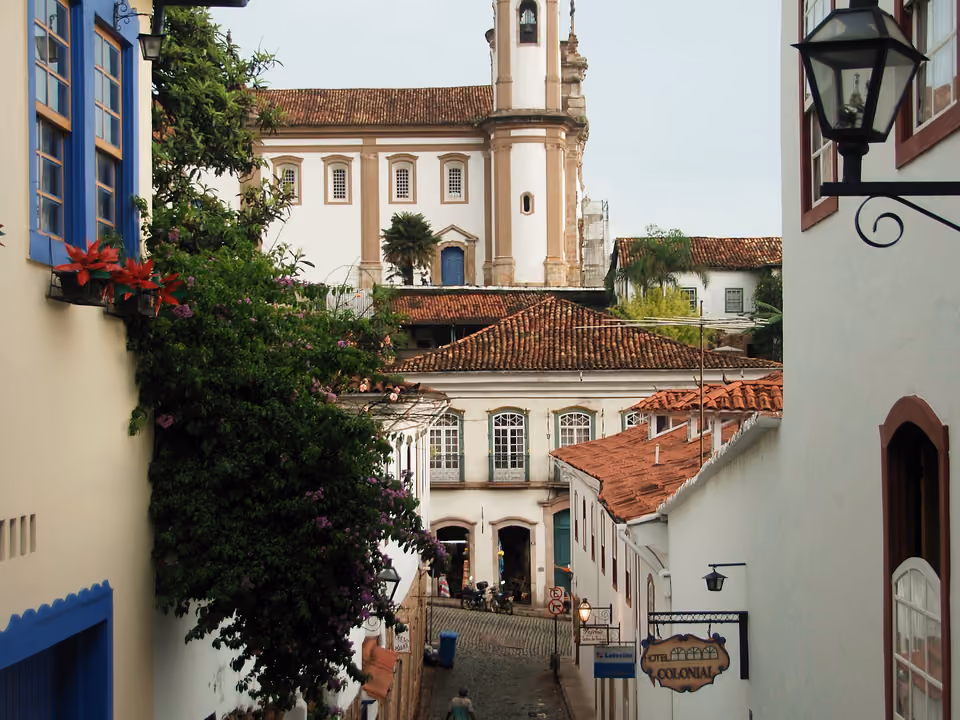 Ladeira estreita de Ouro Preto emoldurada por bougainvíllea florida, com telhados coloniais descendo e a torre da Igreja do Carmo ao fundo