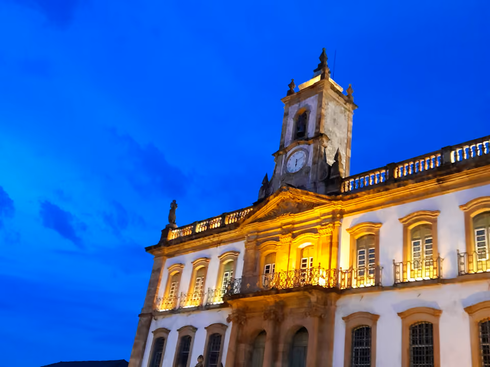 Fachada do Museu da Inconfidência em Ouro Preto ao anoitecer, o antigo prédio branco e caiado da Casa de Câmara e Cadeia com a torre do relógio iluminada contra o céu azul-escuro