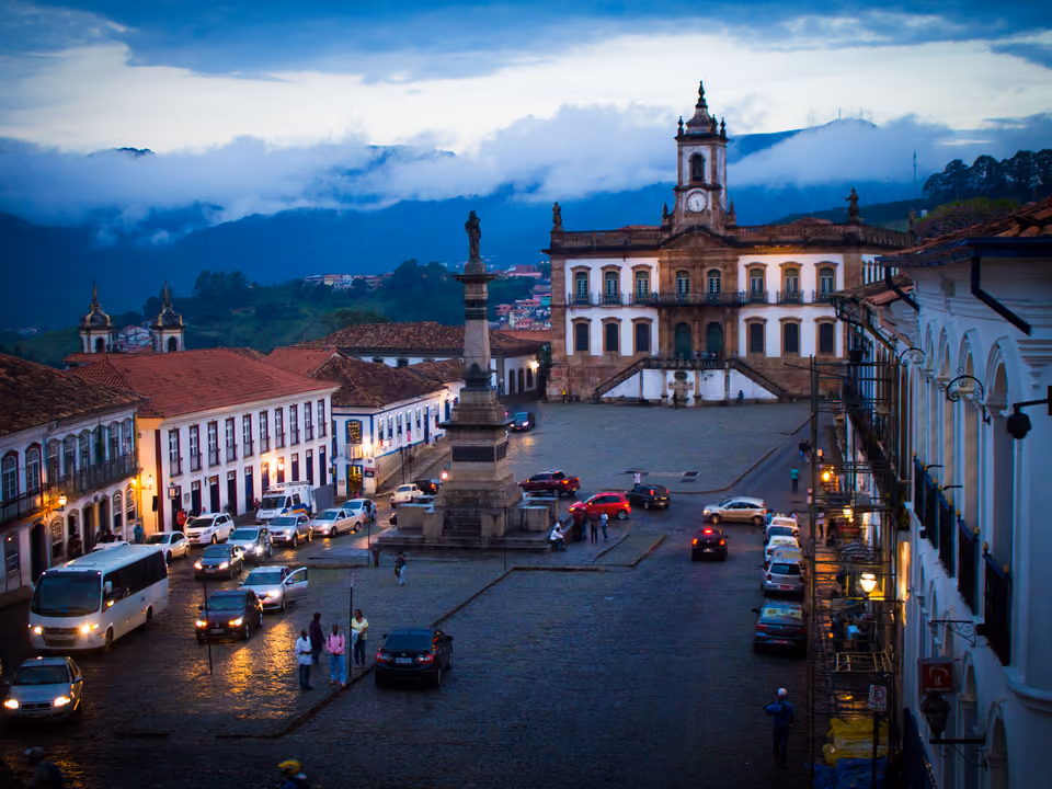 Praça Tiradentes em Ouro Preto ao anoitecer, com o monumento a Tiradentes na coluna central e o Museu da Inconfidência iluminado ao fundo