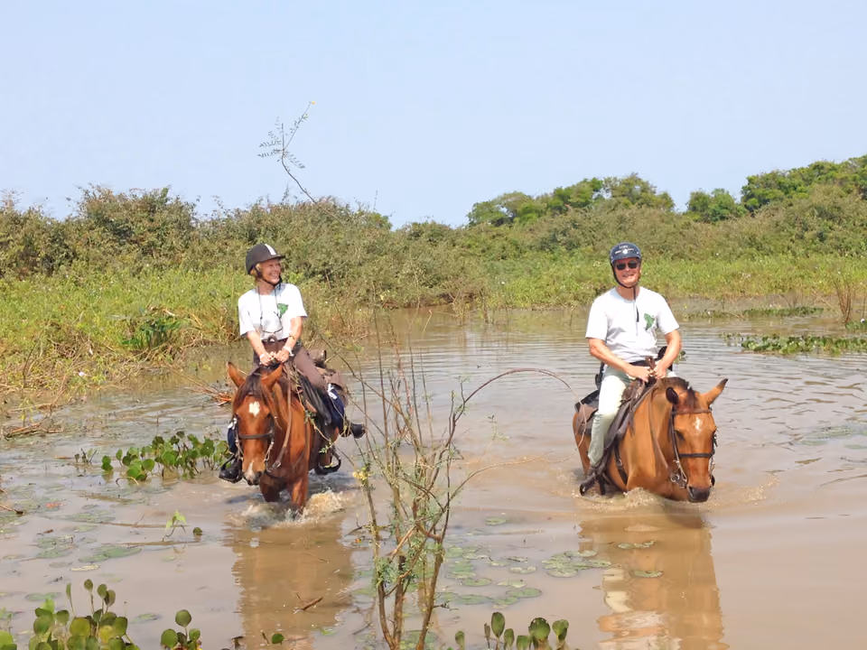 Dois cavaleiros atravessando um trecho alagado do Pantanal a cavalo