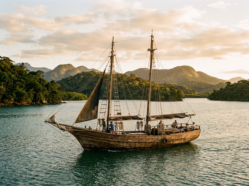 Escuna de dois mastros navegando a baía verde e calma de Paraty entre ilhas de mata