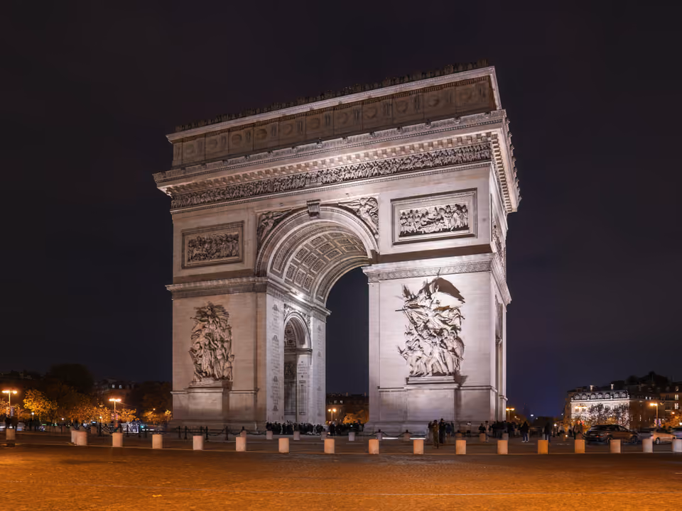 Arco do Triunfo de Paris iluminado à noite, visto em ângulo da praça Charles de Gaulle, com o alto-relevo da Marselhesa na fachada