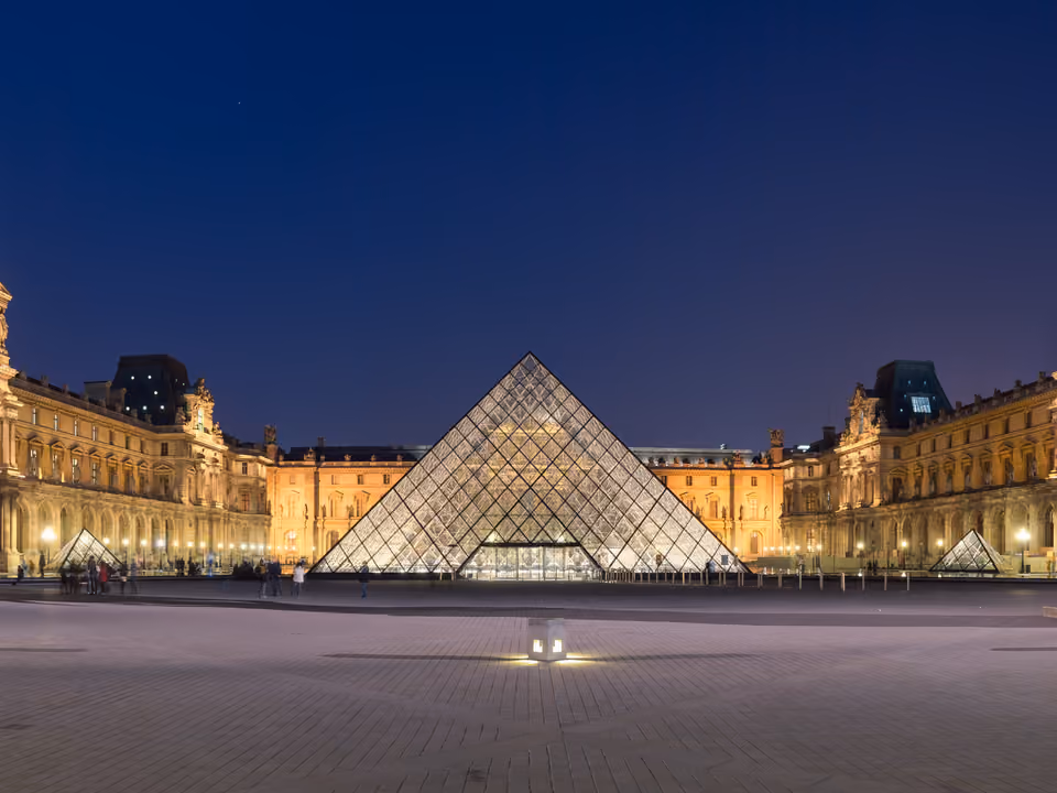 Pirâmide de vidro do Louvre iluminada ao anoitecer no pátio Napoleão, com as alas do palácio ao fundo