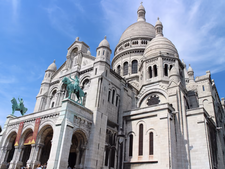 Basílica de Sacré-Cœur de Montmartre vista em ângulo da esplanada, cúpulas brancas sob céu azul e as estátuas equestres na fachada