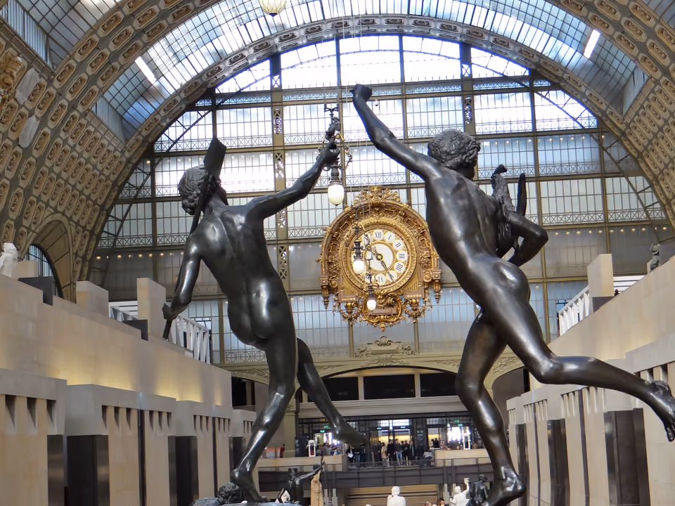 Nave central do Musée d'Orsay, antiga estação de trem, com o grande relógio dourado, o teto de vidro em arco e duas esculturas de bronze em primeiro plano