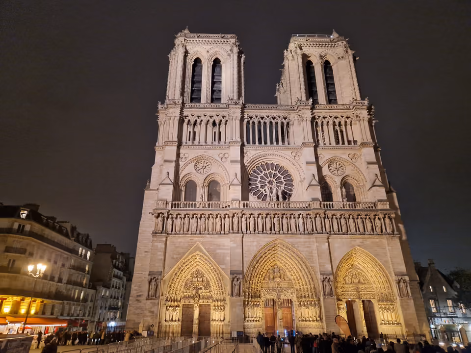 Fachada oeste iluminada da Catedral de Notre-Dame de Paris à noite, com as duas torres, a rosácea e os três portais