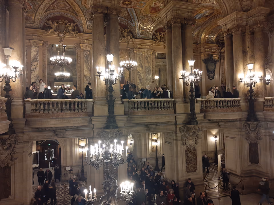 Salão da escadaria monumental da Ópera Garnier, com mármore polido, candelabros, balaústres ornamentados e o teto pintado ao alto