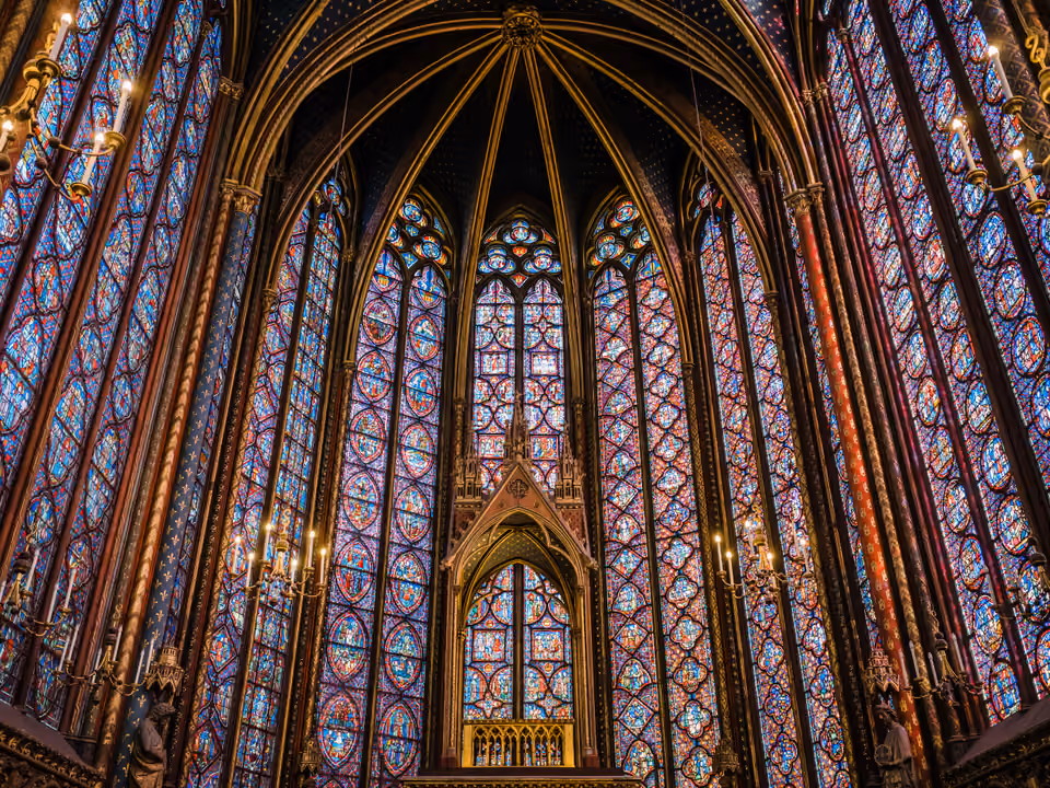 Interior da capela alta da Sainte-Chapelle, paredes quase inteiras de vitrais coloridos entre colunas finas, com o dossel dourado ao centro