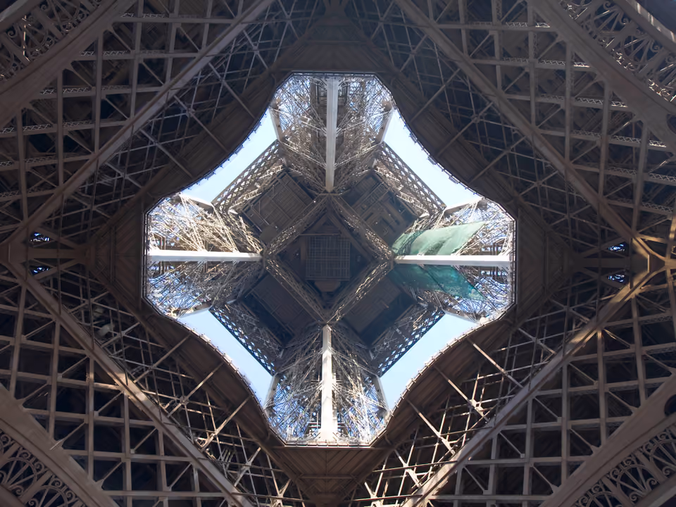 Torre Eiffel vista de baixo, olhando para cima entre os quatro pilares, com a treliça de ferro convergindo contra o céu