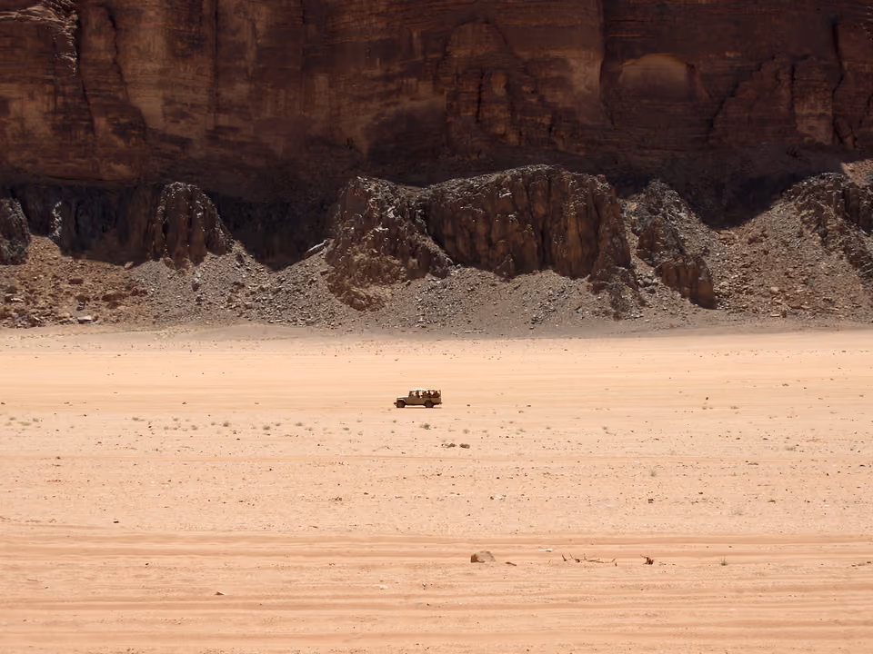 Jipe 4x4 atravessando o deserto avermelhado de Wadi Rum, cercado de formação rochosa, Jordânia