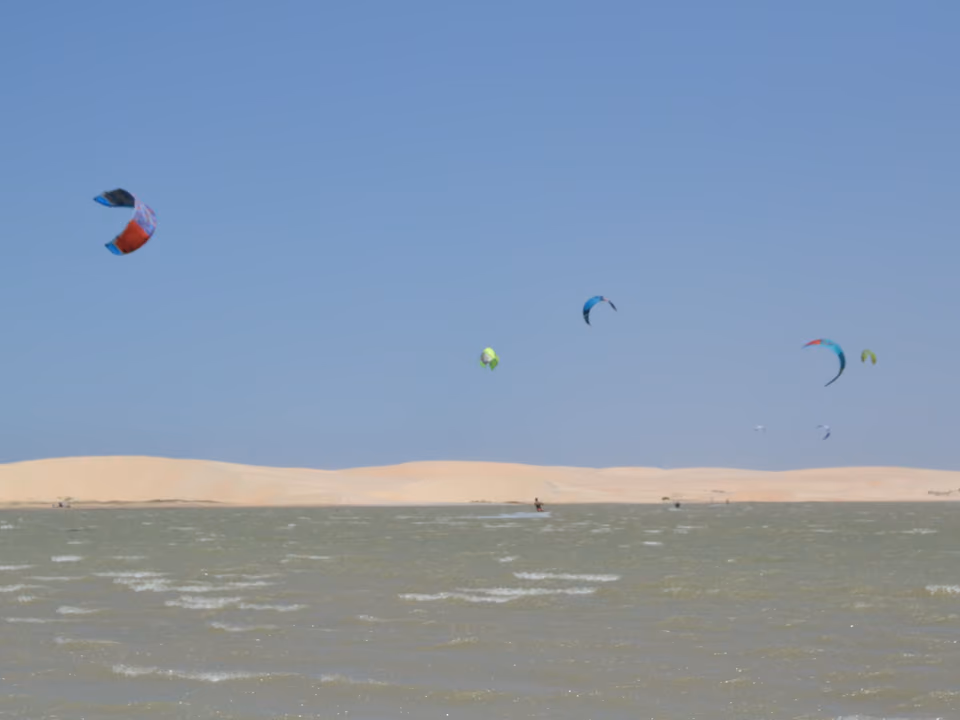 Praticantes de kitesurf sobre lagoa com dunas ao fundo, no litoral do Rio Grande do Norte