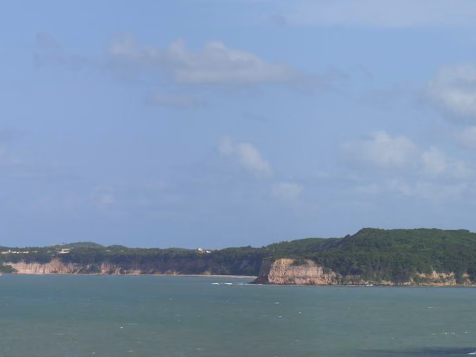Praia do Madeiro, em Pipa, com mar calmo e vegetação de mata ao redor