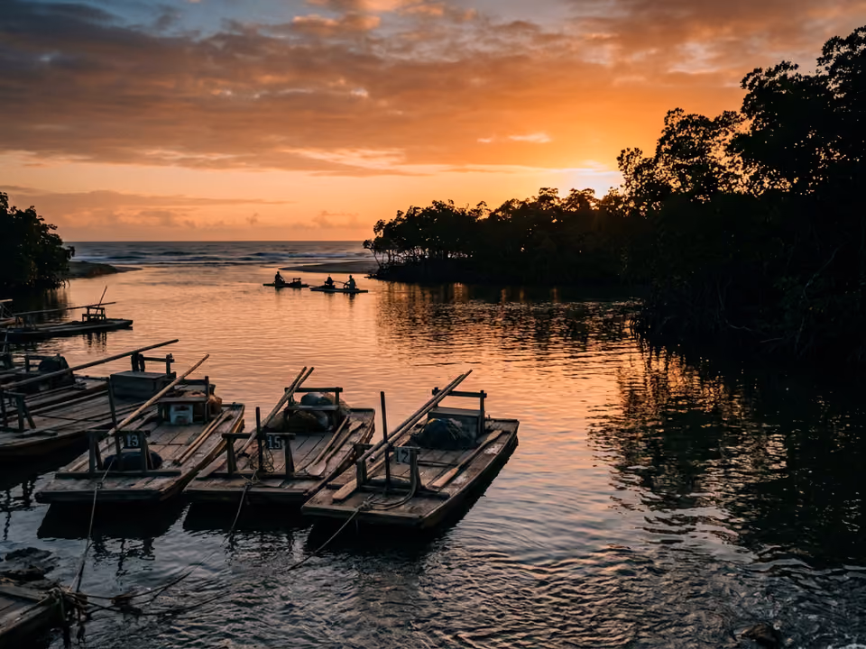 Pôr do sol laranja no Pontal de Maracaípe, com jangadas no encontro calmo do rio com o mar