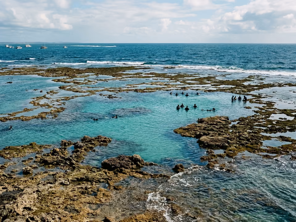 Piscinas naturais turquesa do Recife de Fora na maré baixa, com silhuetas distantes de snorkel