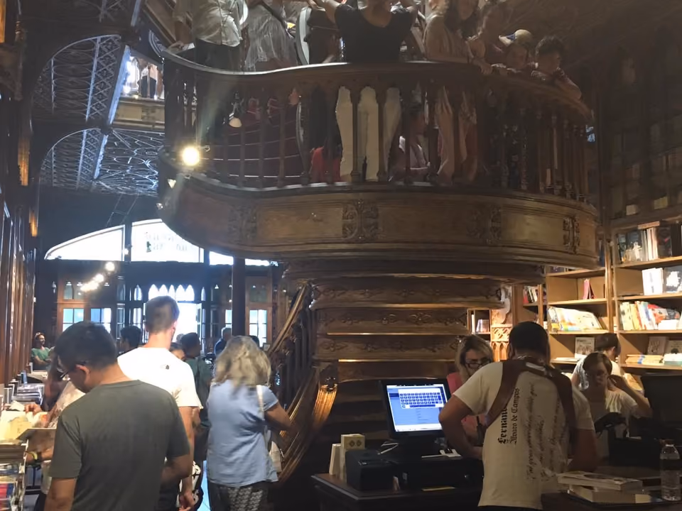 Interior da Livraria Lello em Porto, com a escadaria vermelha curva e o teto de vitral entalhado