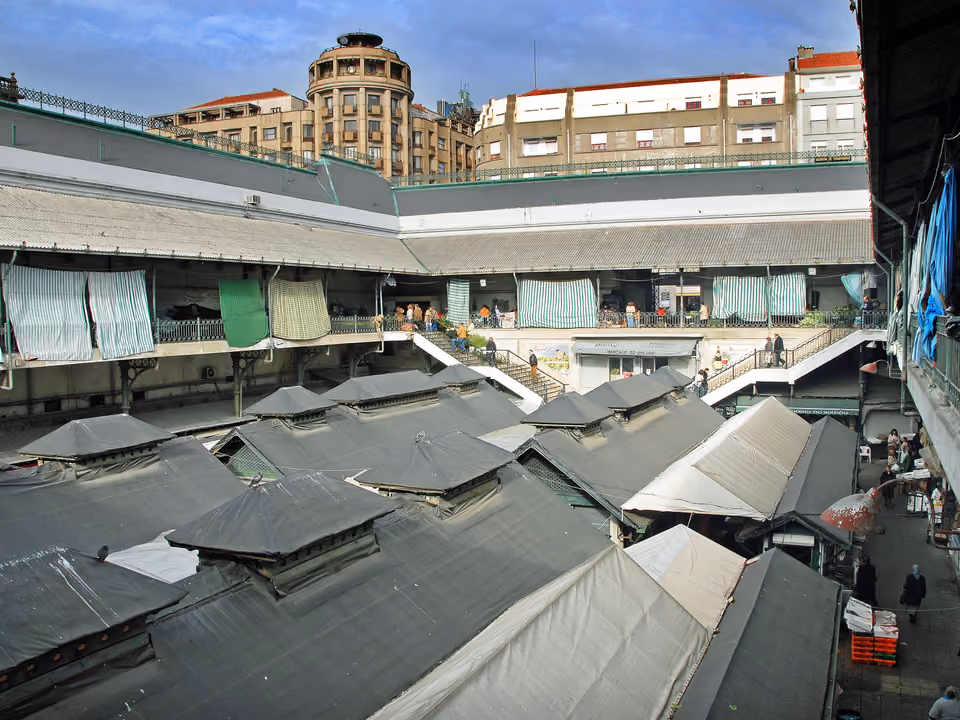 Interior do Mercado do Bolhão em Porto, com barracas de frutas, peixe e flores sob a estrutura de ferro reformada
