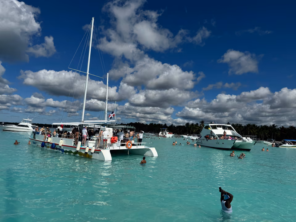 Catamarã de passeio ancorado em água turquesa rasa, com turistas nadando ao redor