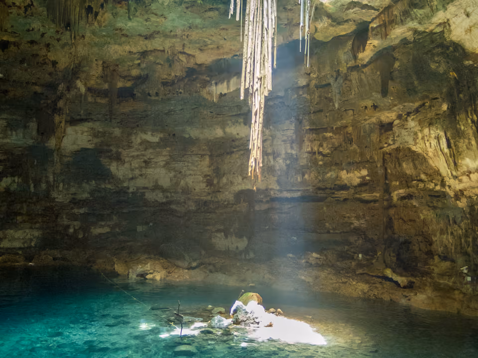 Cenote de água doce turquesa dentro de uma caverna de rocha calcária, com raízes penduradas do teto