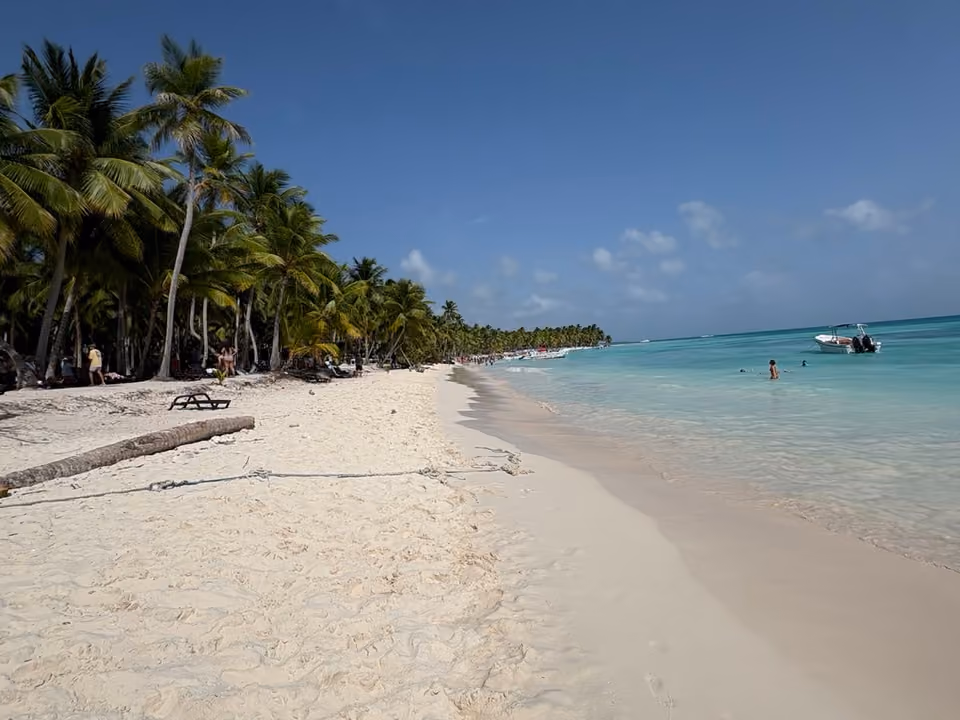 Praia de areia branca e coqueiros na Ilha Saona, com um pequeno barco ancorado na água turquesa