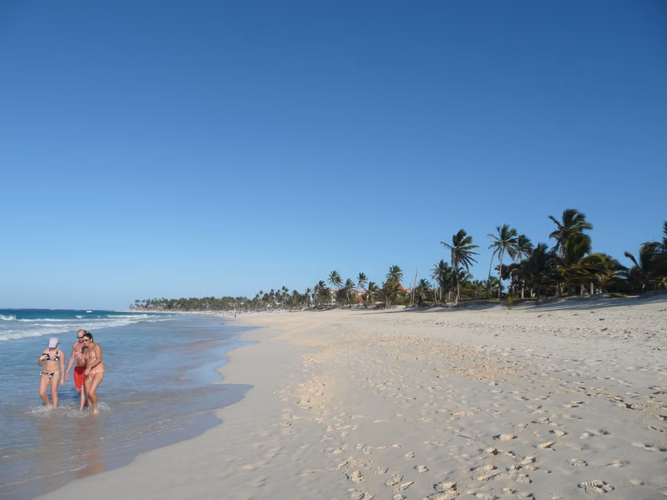 Trecho da orla de Punta Cana com banhistas e coqueiros, ilustrando a paisagem fora das áreas de resort