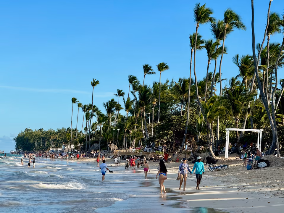 Faixa de areia da Playa Bávaro com banhistas caminhando pela orla e coqueiros ao fundo