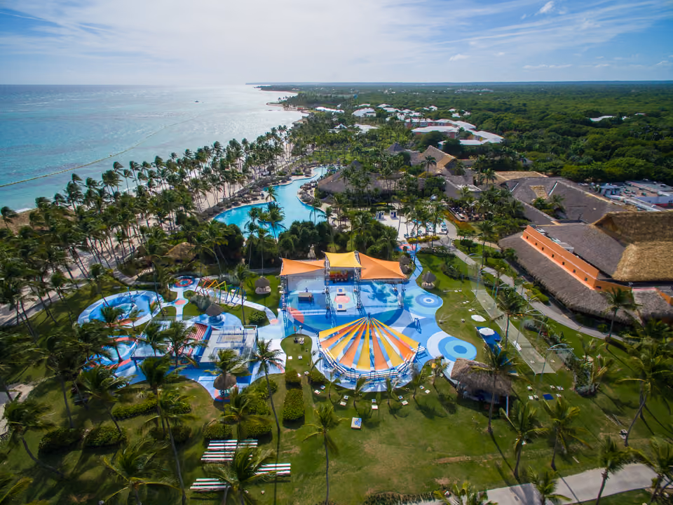Vista aérea de um resort all-inclusive em Punta Cana, com piscinas, área de lazer e coqueiros até a praia